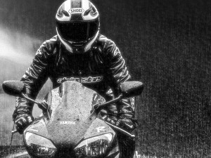 Motorcyclist riding in the rain wearing a leather jacket.